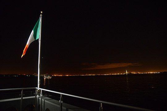 Irish Flag at Pier A at night. In the background is Ellis Island. Credit: James Higgins