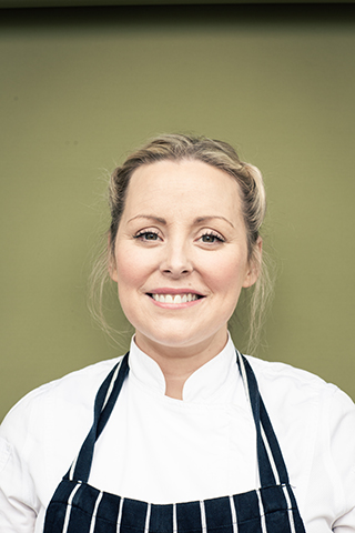 Celebrity chef Anna Haugh - headshot of a blonde woman wearing her hair tied back and a navy and white striped chef's apron.