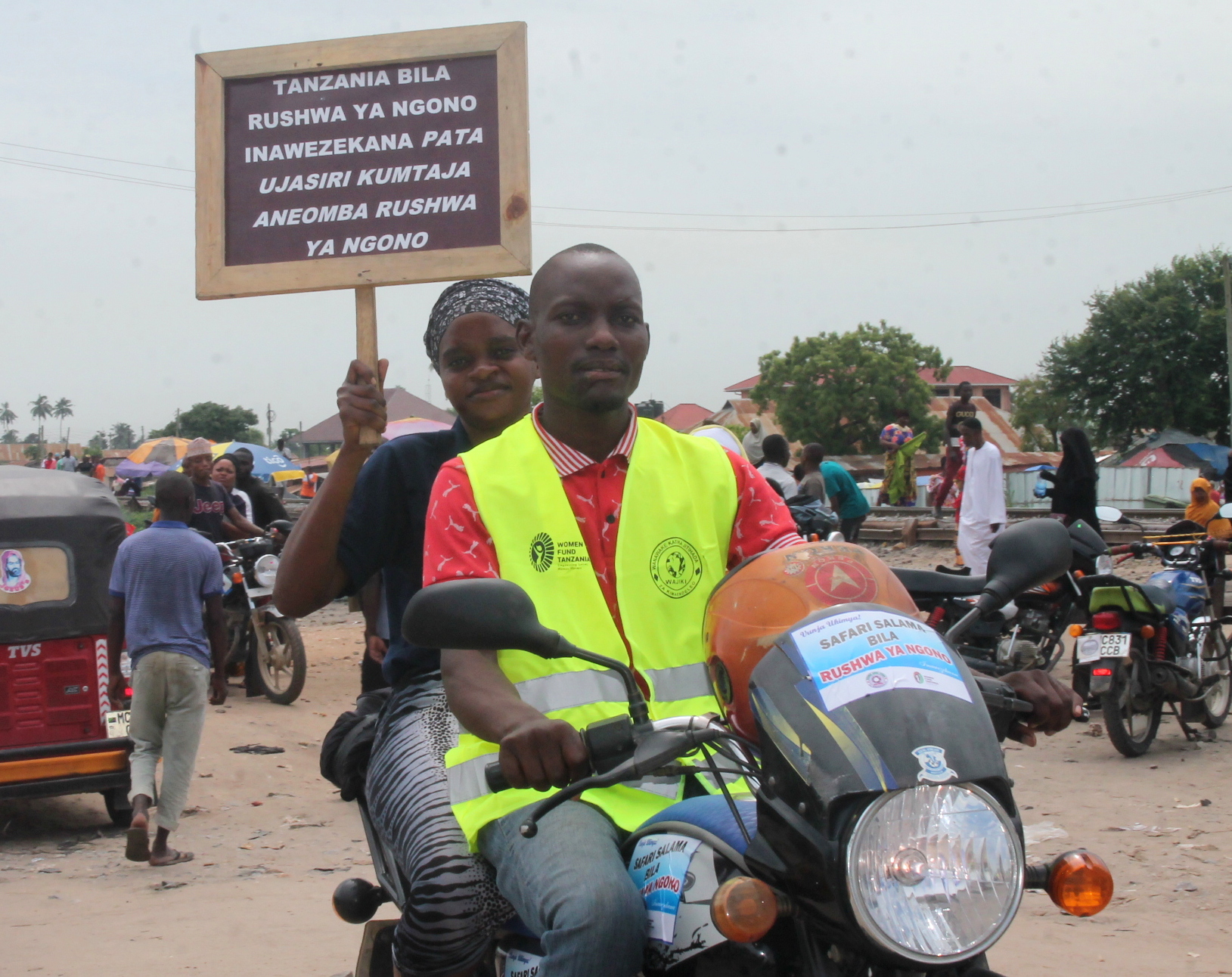 A woman on a bodaboda proudly holds a sign during phase 3 of WAJIKI’s Break the silence, Safe travel for girls without Sextortion in Kinondoni and Temeke Districts.